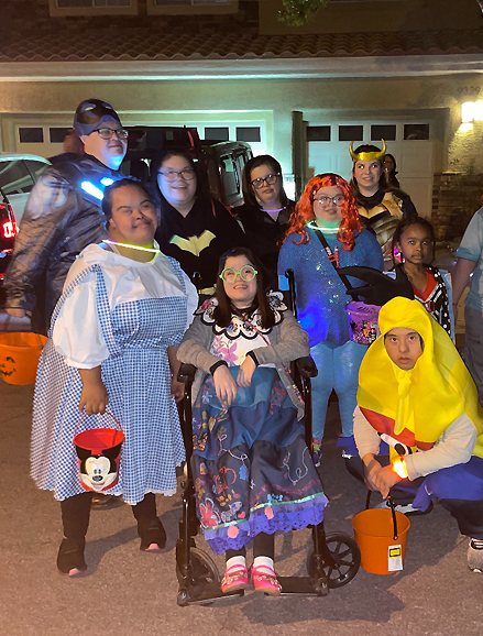 Members in Halloween costumes with trick-or-treat buckets outside a house at night.