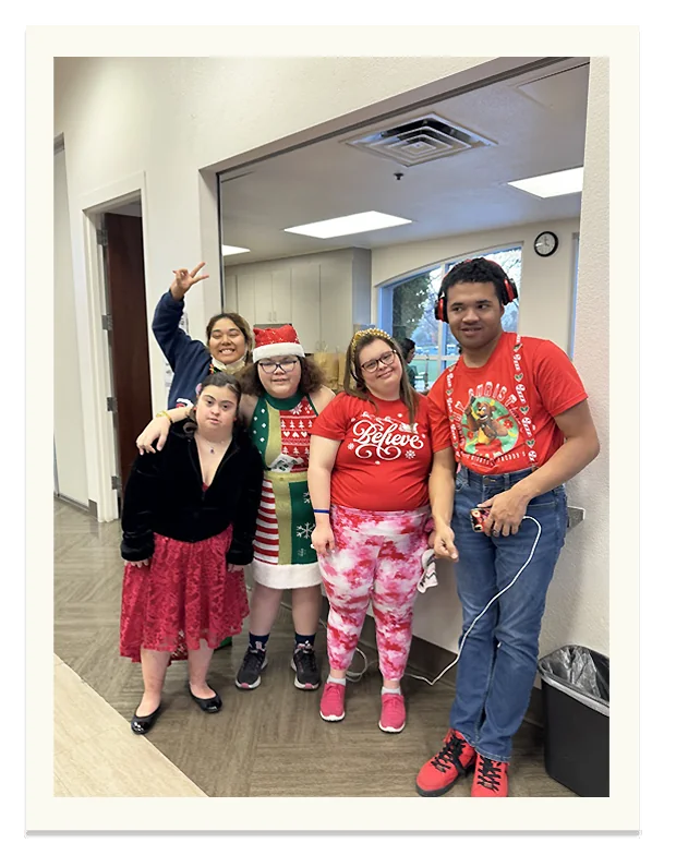 Five members in festive holiday sweaters posing together with big smiles.